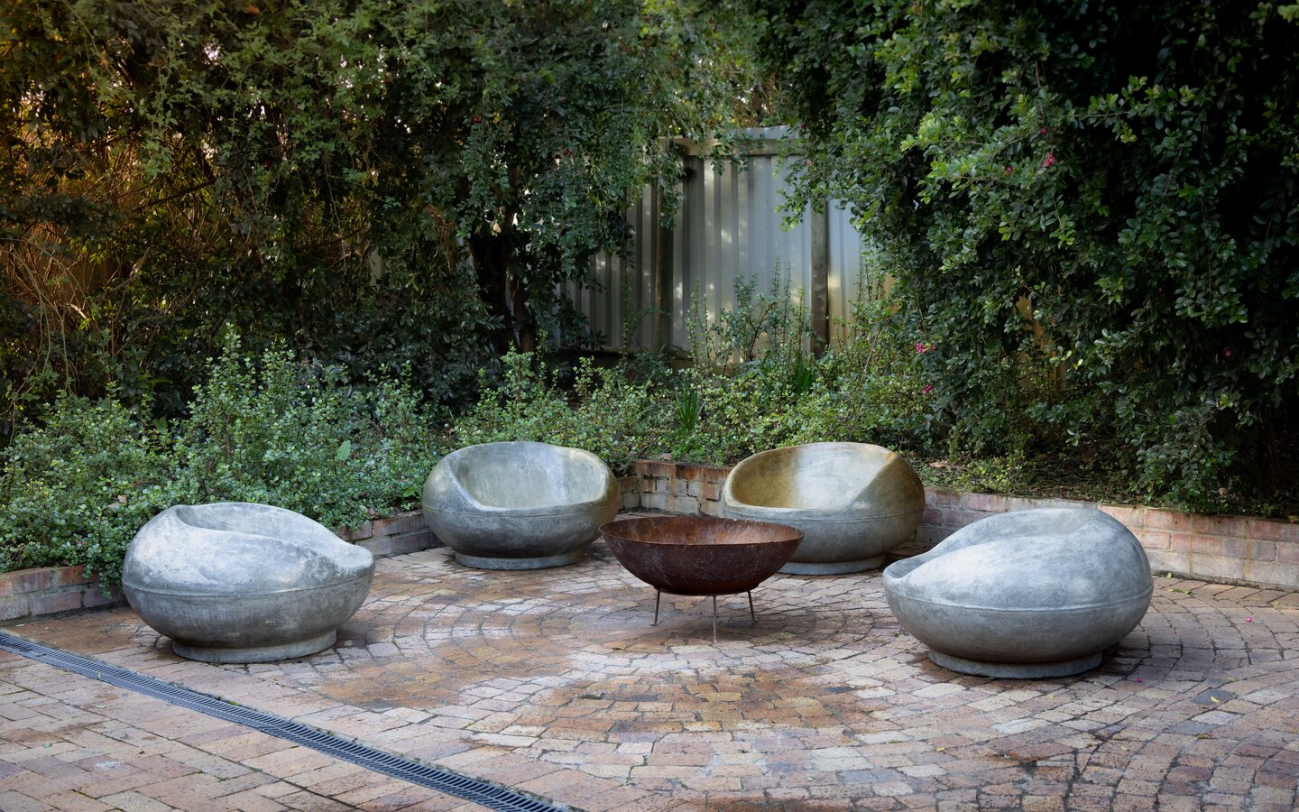 A thoughtfully arranged outdoor patio with stone seating, a fire pit, and layered greenery.